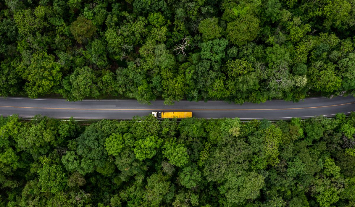 Flygfoto av gul lastbil som kör genom en väg i skogen.